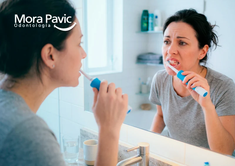 Mujer cepillándose los dientes con sangrado de encías frente al espejo, señal de posible enfermedad periodontal